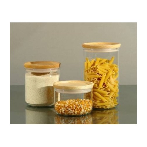 Tres tarros herméticos con tapa de madera llenos de pasta, palomitas de maíz y harina sobre una superficie reflectante.