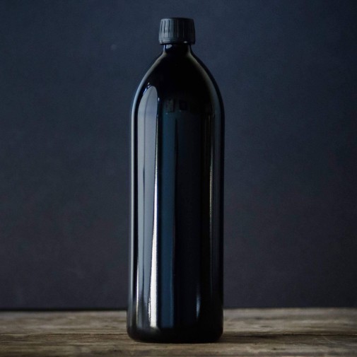 Botella alta de vidrio Miron Violeta sobre superficie de madera con fondo oscuro.