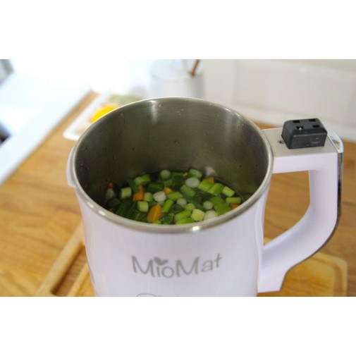 Licuadora abierta MioMat con vegetales picados, ideal para leches vegetales saludables, sobre encimera.
