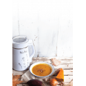 Sopa de calabaza en un bol, rodeada de rodajas de calabaza y una máquina de leches vegetales saludables.