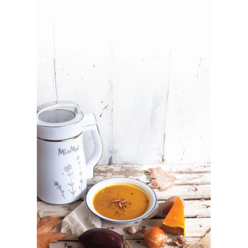 Sopa de calabaza en un bol, rodeada de rodajas de calabaza y una máquina de leches vegetales saludables.