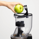 Mano colocando una manzana verde en un exprimidor Kuvings CS600 para obtener zumos frescos.