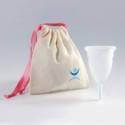 Copa menstrual al lado de una bolsa con cordón y una cinta rosa sobre fondo gris.