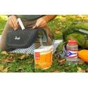 Persona vertiendo agua en una bolsa de comida Pad Thai al aire libre, rodeada de equipos de cocina solar.