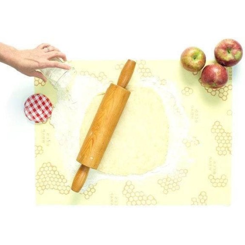 Bee’s Wrap sobre masa, rodillo en posición vertical, manzanas y un frasco para darle un toque ecológico.