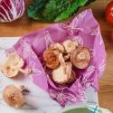 Hongos y verduras sobre un envoltorio de abeja con estampado morado encima de una superficie de madera.