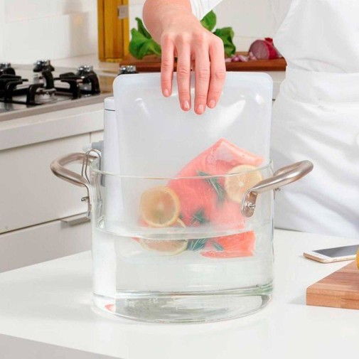 Persona colocando una bolsa de silicona reutilizable con salmón en una olla con agua para cocinarlo al vacío.