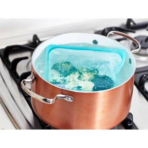 Bolsa hermética de silicona platino con verduras hirviendo en una olla de cobre sobre una estufa.