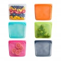 Seis bolsas de silicona reutilizables de colores, una con fruta, otra hermética con coles de Bruselas.