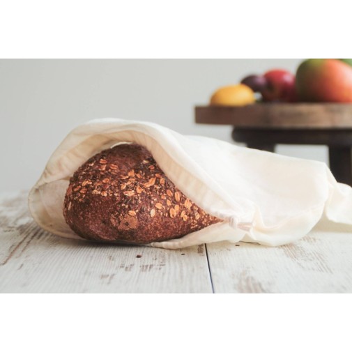 Hogaza de pan en una bolsa de algodón ecológico sobre una mesa, con frutas de fondo.