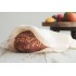 Hogaza de pan en una bolsa de algodón ecológico sobre una mesa, con frutas de fondo.