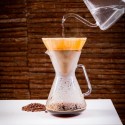 Cafetera de goteo de vidrio en uso, con agua vertiéndose sobre café molido.