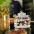 Tetera de cristal con agua humeante, perfecta para café o infusiones, sobre superficie reflectante.