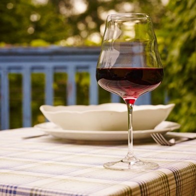 Copa de vino sobre mantel a cuadros con un toque de vino tinto, plato blanco de fondo.