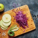 Manzana en rodajas, repollo morado y pepino cortados con mandolina sobre una tabla de madera.