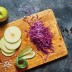 Manzana en rodajas, repollo morado y pepino cortados con mandolina sobre una tabla de madera.