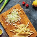 Cebollas y patatas picadas sobre una tabla de madera con frutas y verduras, limón y aceite cerca.