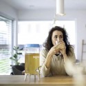 Mujer bebiendo una bebida de un vaso en una mesa con un dispensador de bebidas cerca.