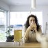 Mujer bebiendo una bebida de un vaso en una mesa con un dispensador de bebidas cerca.