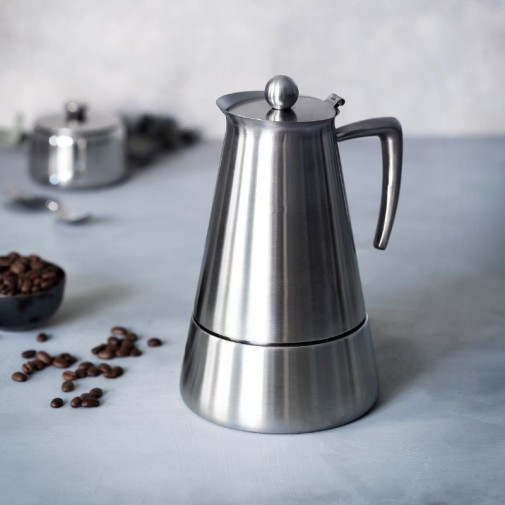 Cafetera Express de acero inoxidable con granos de café esparcidos alrededor.