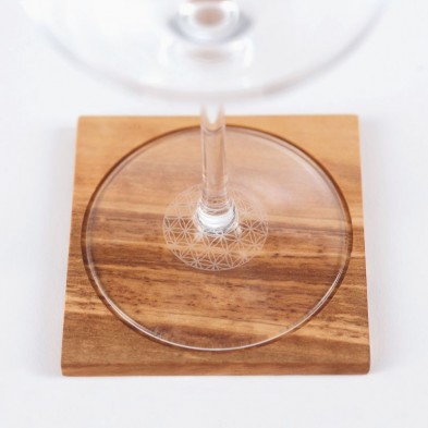 Copa de vino sobre posavasos de madera con motivos geométricos de la flor de la vida