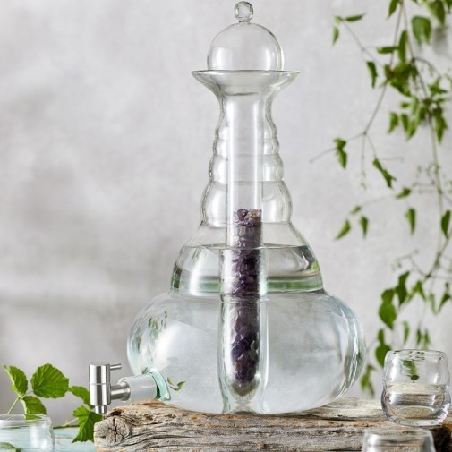 Elegante dispensador de agua de vidrio Beauty de 5L, con cristal en su interior, sobre madera rústica, rodeado de hojas.