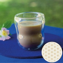 Un vaso doble pared de borosilicato con café y diseño geométrico sobre un tapete azul.