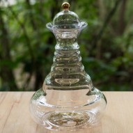 Elegante jarra vitalizadora de vidrio con tapón oro 24 quilates y diseño del árbol de la vida sobre una mesa de madera.