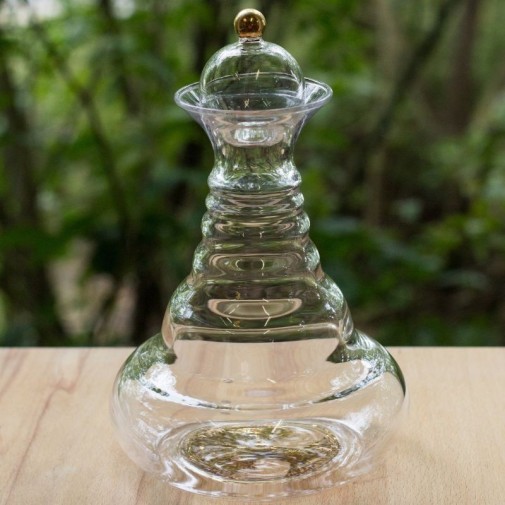 Elegante jarra vitalizadora de vidrio con tapón oro 24 quilates y diseño del árbol de la vida sobre una mesa de madera.