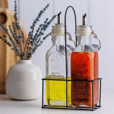 Dos botellas de vidrio con aceite y vinagre en un soporte de metal sobre la encimera de la cocina.