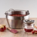 Olla para hacer mermeladas Kilner con fresas, un frasco, un colador, una espátula y frascos de mermelada sobre una mesa.