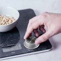Una mano pulsando el botón econmove de la balanza digital de cocina con un bol de piñones.