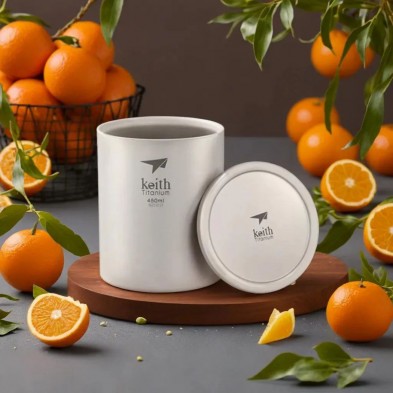 Taza de titanio doble pared y tapa 450 ml Keith en una encimera con naranjas