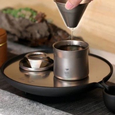 Una mano vierte líquido a través del embudo del mini kit cafetera tetera Keith, sobre una bandeja.