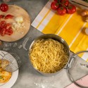 La olla ALLROUND llena de espaguetis cocidos rodeada de ingredientes y utensilios de cocina sobre una encimera.
