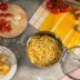 La olla ALLROUND llena de espaguetis cocidos rodeada de ingredientes y utensilios de cocina sobre una encimera.