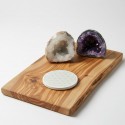 Posavasos vitalizador de piedra con la Flor de la vida sobre tabla de cortar de madera y dos geodas