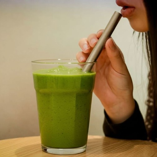 Una chica bebiendo un batido verde con la Pajita titanio ancha Keith