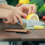 Cuchillo de titanio pequeño Keith con funda de cuero sobre la mesa y cortando con él una rodaja de limón
