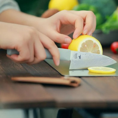 Cuchillo de titanio pequeño Keith con funda de cuero sobre la mesa y cortando con él una rodaja de limón Cuchillo de titanio pequeño Keith con funda de cuero sobre la mesa y cortando con él una rodaja de limón