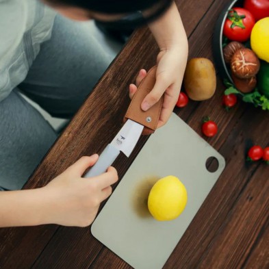 Sacando el cuchillo de titanio pequeño Keith de la funda sobre una encimera de cocina de madera Sacando el cuchillo de titanio pequeño Keith de la funda sobre una encimera de cocina de madera