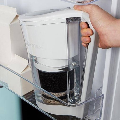 Mano sosteniendo una jarra con filtro de agua Alkaplus en el estante de la puerta del refrigerador.
