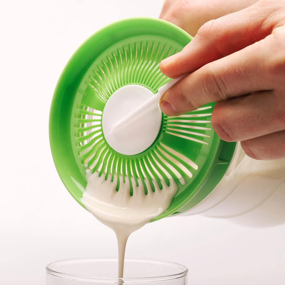 Kéfir de leche colándose por la tapa colador de Kefirko hacia un vaso